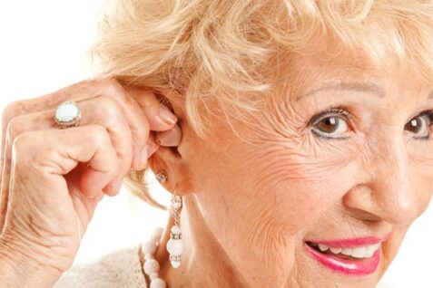 Closeup of A Senior Woman Inserting Hearing Aid In Her Ear.