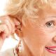Closeup of A Senior Woman Inserting Hearing Aid In Her Ear.