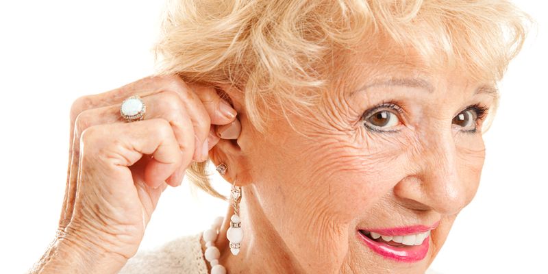 Closeup of A Senior Woman Inserting Hearing Aid In Her Ear.