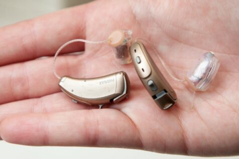 A Man Holding Hearing Aid Parts In His Hand.