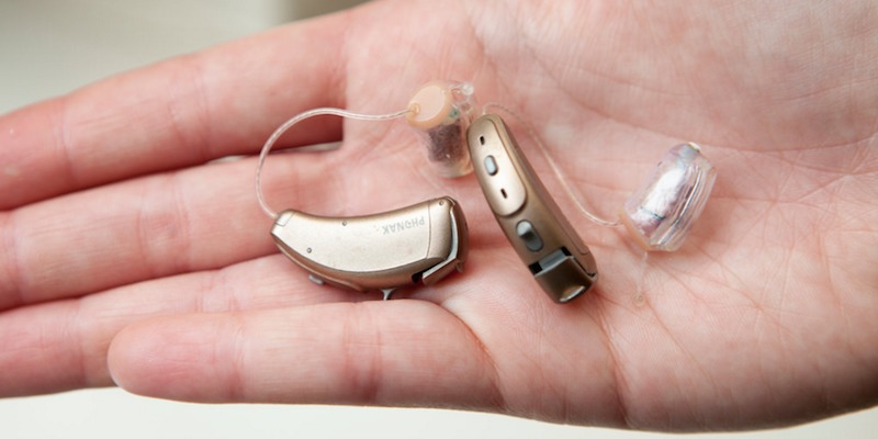 A Man Holding Hearing Aid Parts In His Hand.