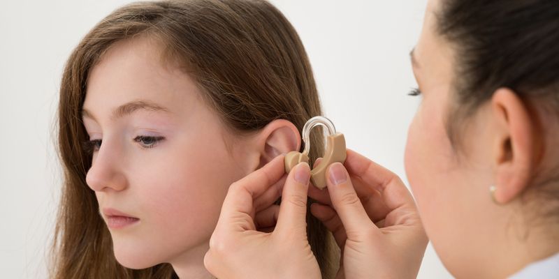 A Doctor Putting Hearing Aid In The Ear of A Girl.